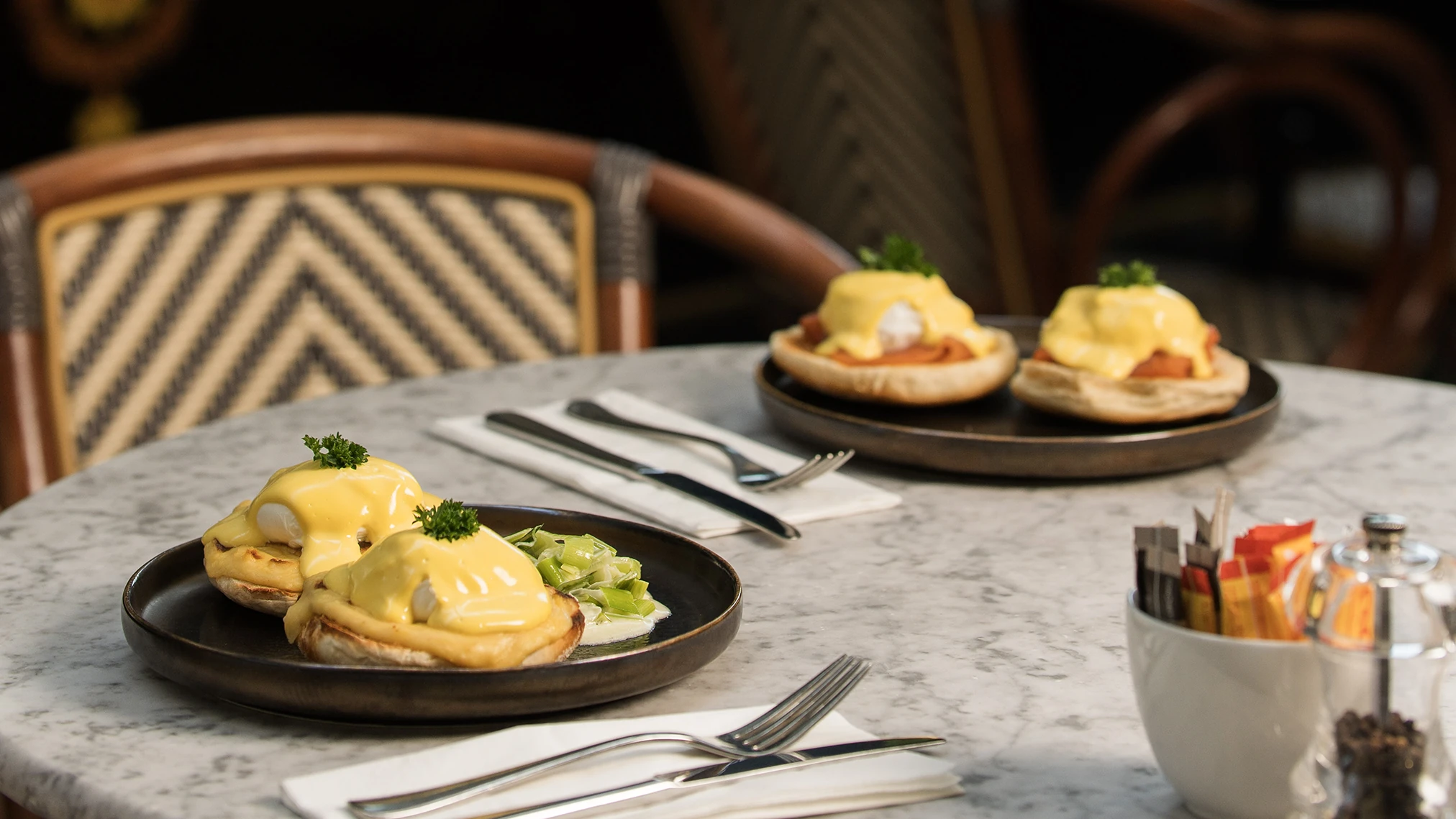 Plates of Eggs Benedict on a marble cafe table.