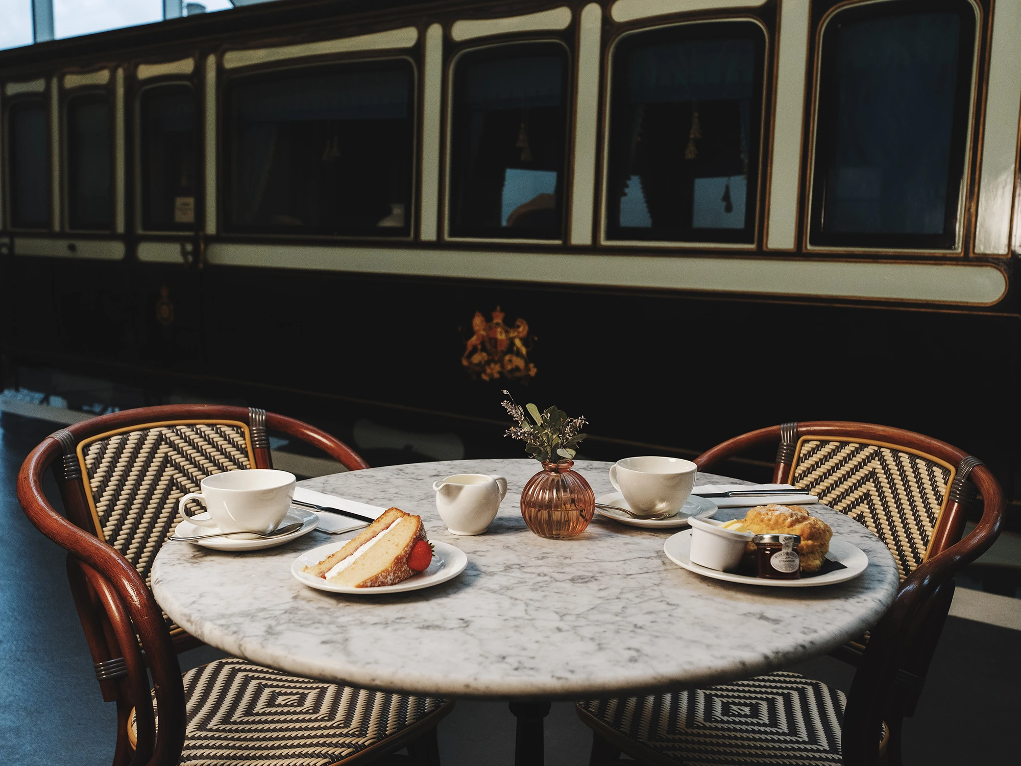 Marble table setting with cake and tea in front of a vintage train carriage.