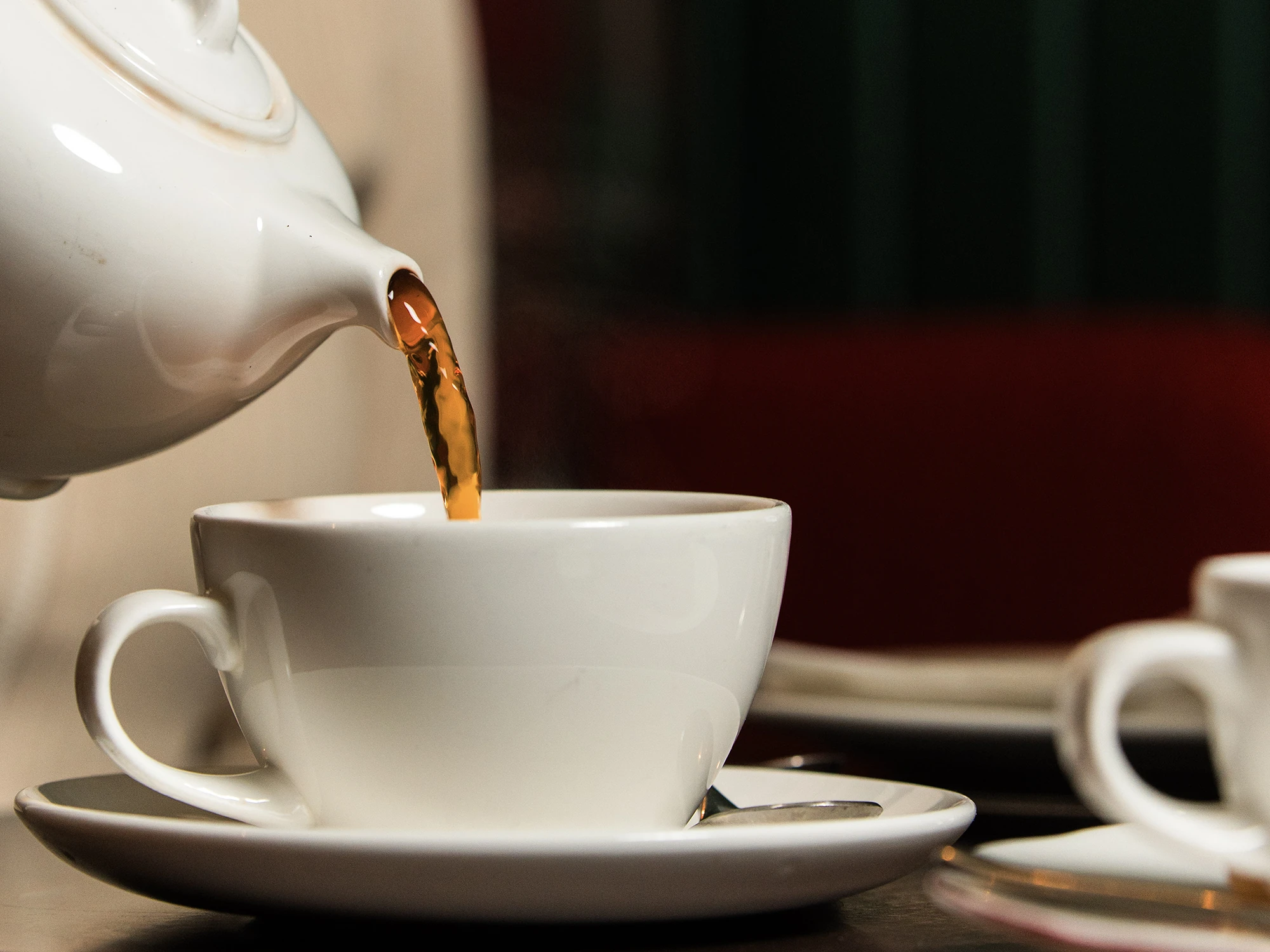 Tea being poured from a white teapot into a cup.